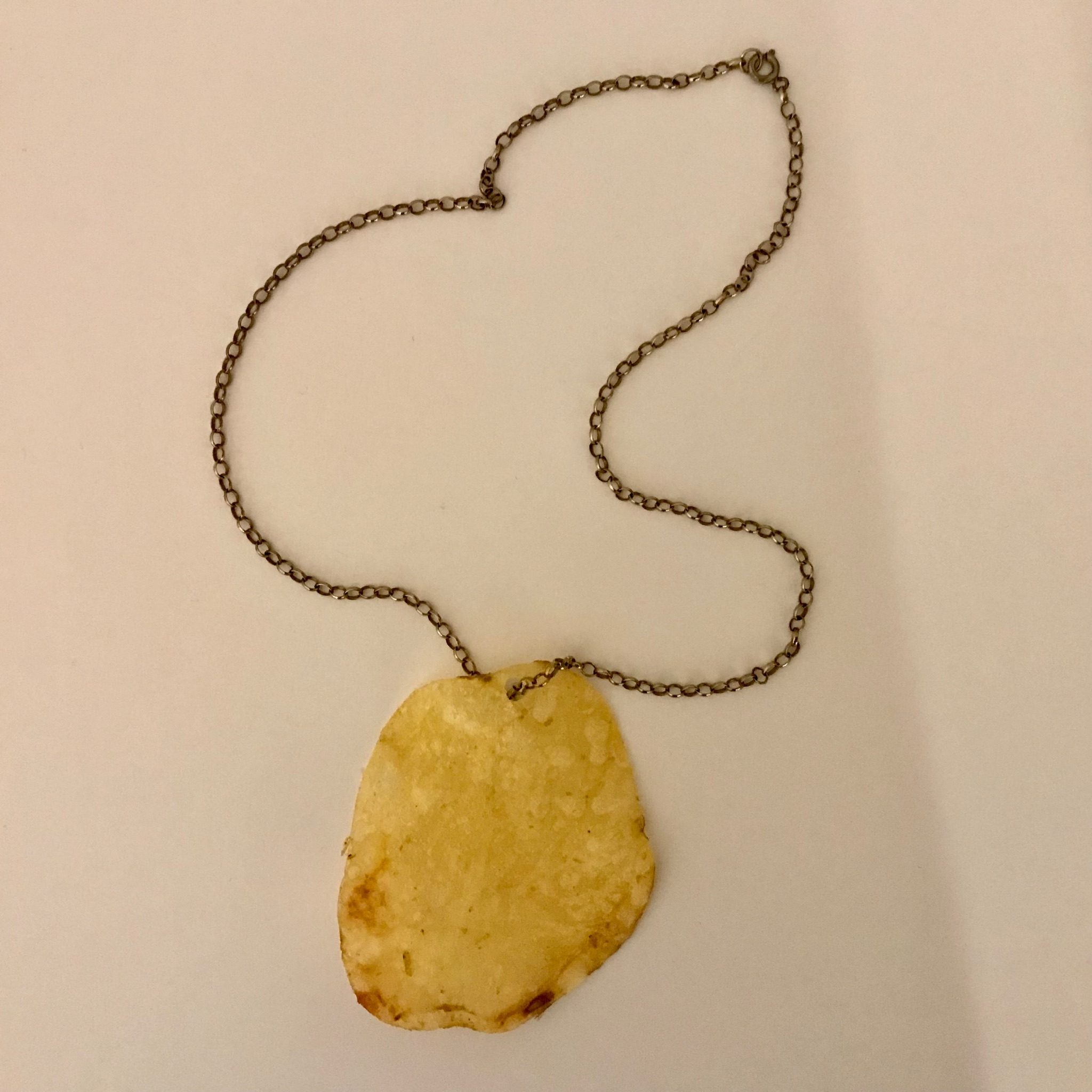 A photograph of a carefully pierced potato crisp threaded onto a necklace