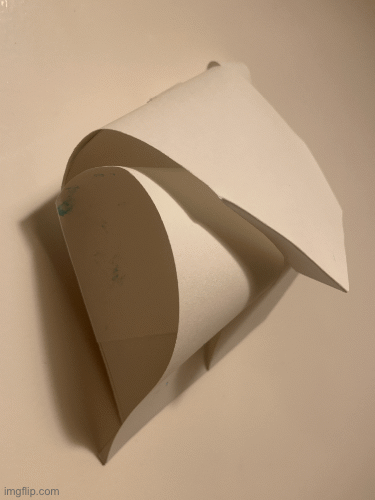 paper sculpture with two sides, one with cut shapes and bends, the other with blue glued joints and a large sweep of space protruding towards the viewer followed by a small page of text.