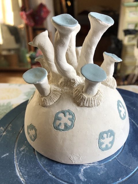 2nd stage of a porcelain work: addition of turquoise engobe on the corollas surmounting stems. the work is a half sphere from which come out outgrowths surmounted by corollas.