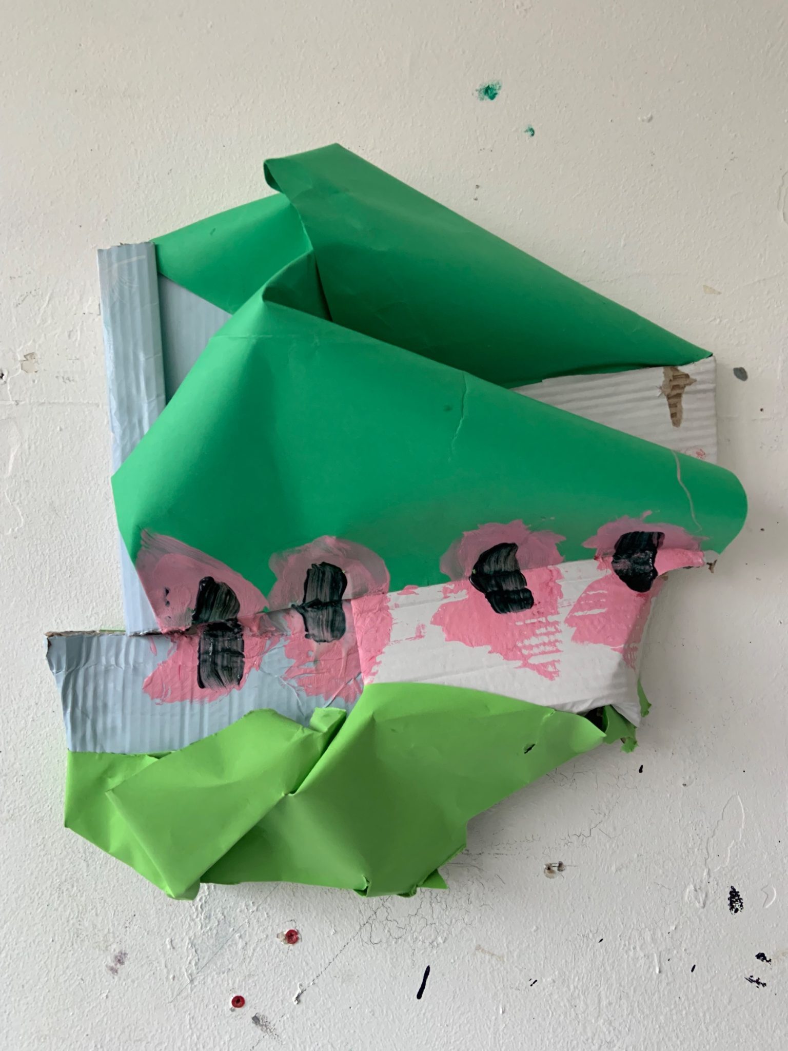 sculpture made from green dark on top, blue and white cardboard in the middle, and like green cardboard on bottom, with paint marks sealing the green top bit down to the cardboard. overall shape reminiscent of a ship.