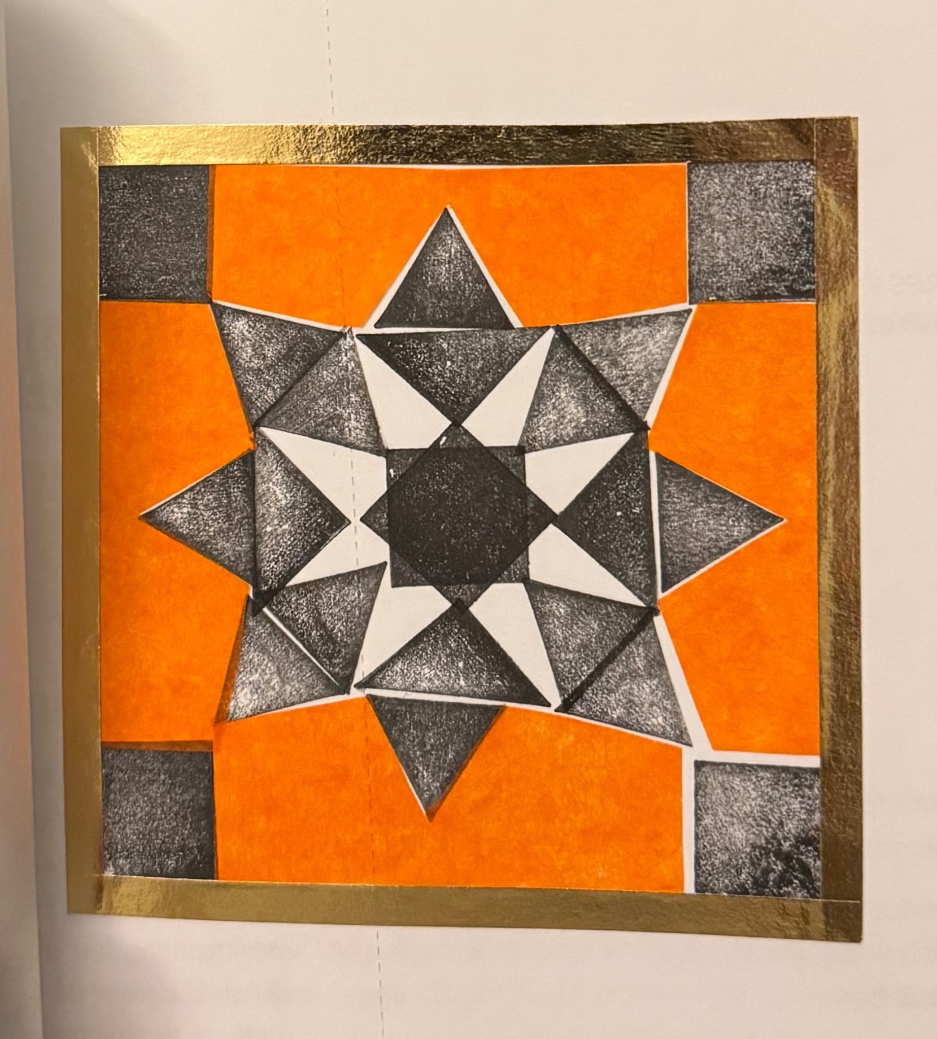 Black and white shapes forming a pattern with coloured tissue paper in a golden tape frame.