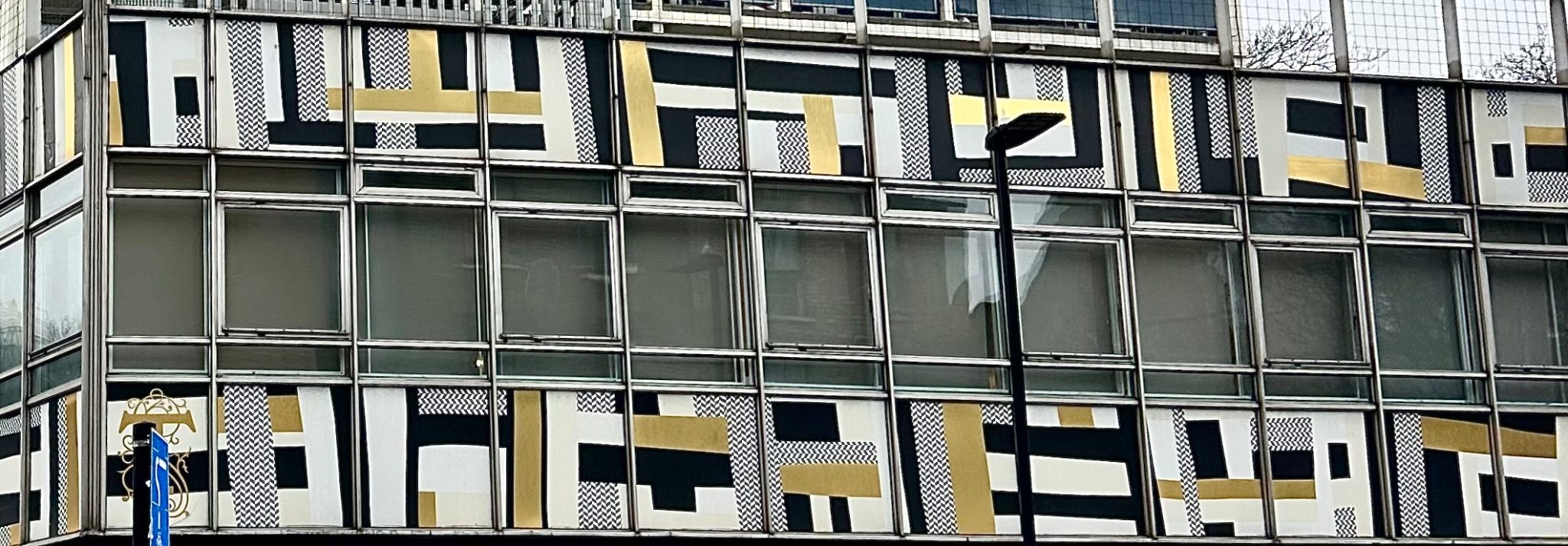 Photograph. Graphic mural on building in multiple progressing variations of black white and gold shapes