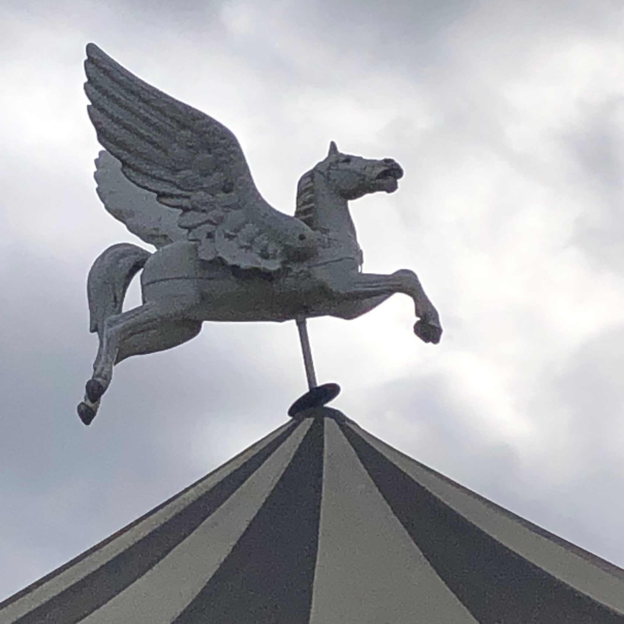 Photo of the top of the tent of a merry-go-round, with the statue of a winged horse at the top. All in white and gray