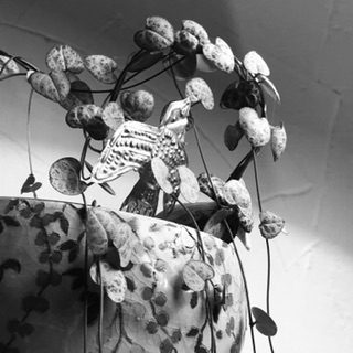 Black and white photo: a rounded ceramic receives a small leaf plant in the shape of a heart, a bird in the middle in pushed aluminum