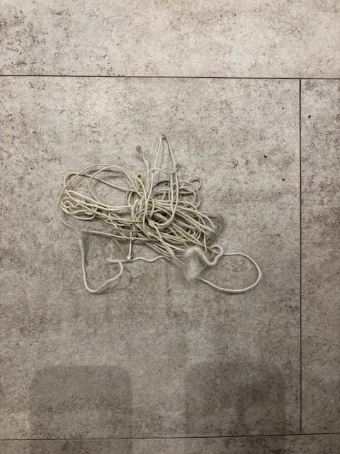 Photo of tangled length of string on grey background. Two shadows, maybe seats, facing scene. Contasted with clean dark straight lines