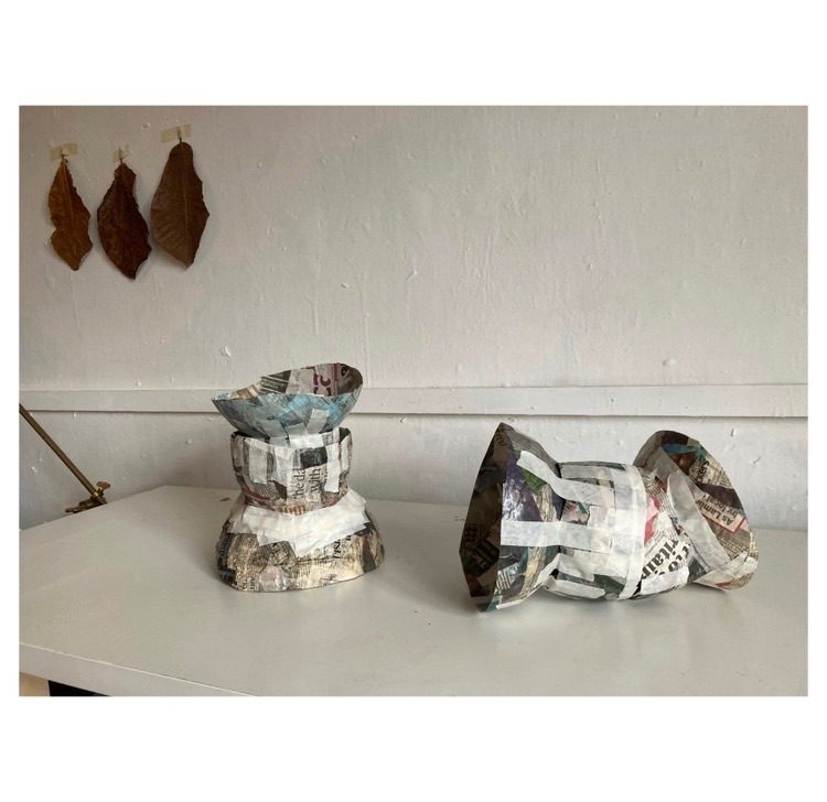 Papier-mache forms on a table with 3 giant leaves in the background