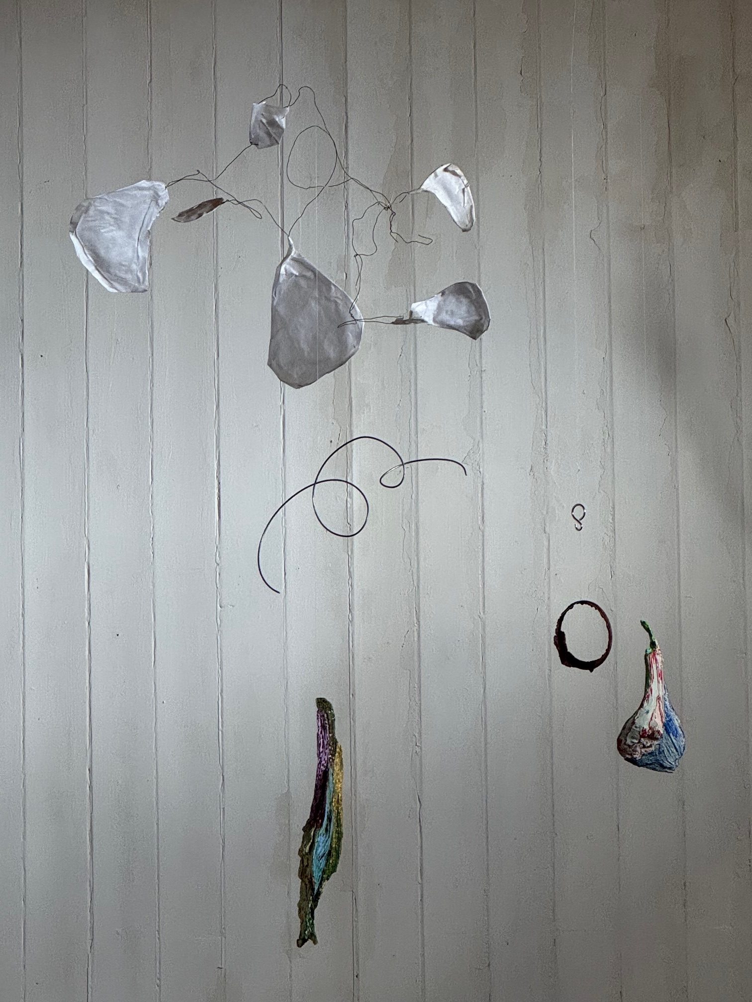 Bits and pieces hanged with fish strings in front of a white wall. Curled wires, Japanese paper glued onto wire shapes, painted wood