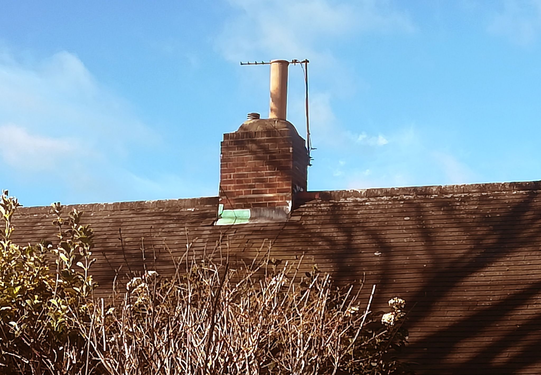 shadow of a tree falling on long low flat former alms house, central chimney pot catching sunlight. Photographed from bedroom window
