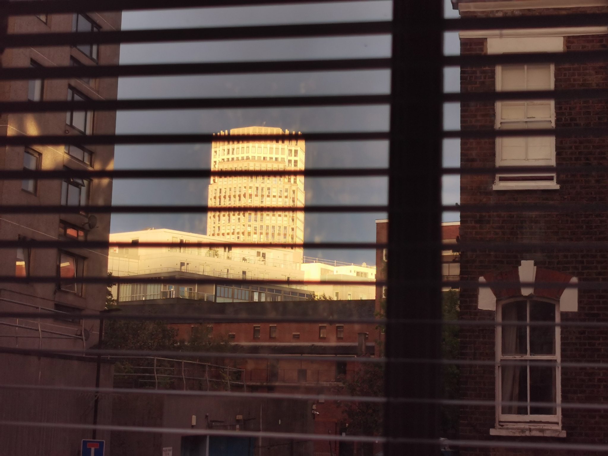 An office block reflects sunlight turning it white between dark buildings