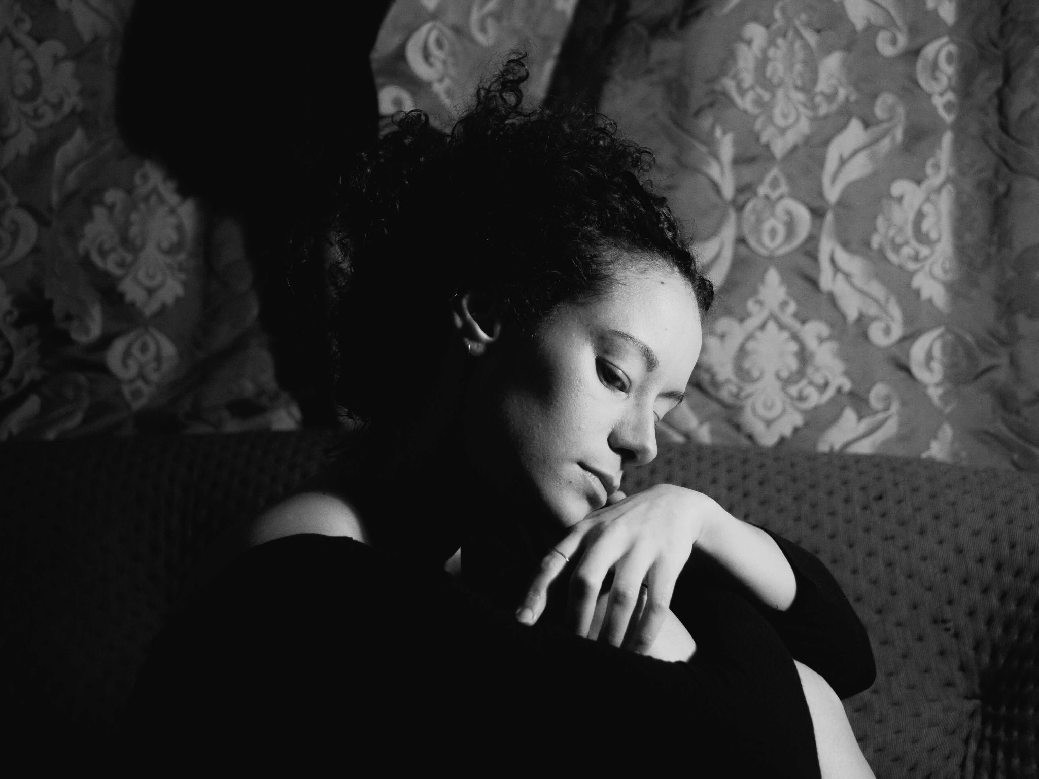A black and white self-portrait, pensive expression against soft furnishings