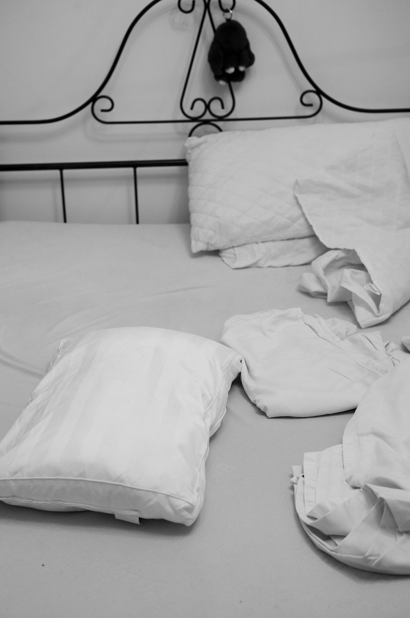 Black and White image of an unmade bed. Fresh sheets and pillowcases being put onto a bed.