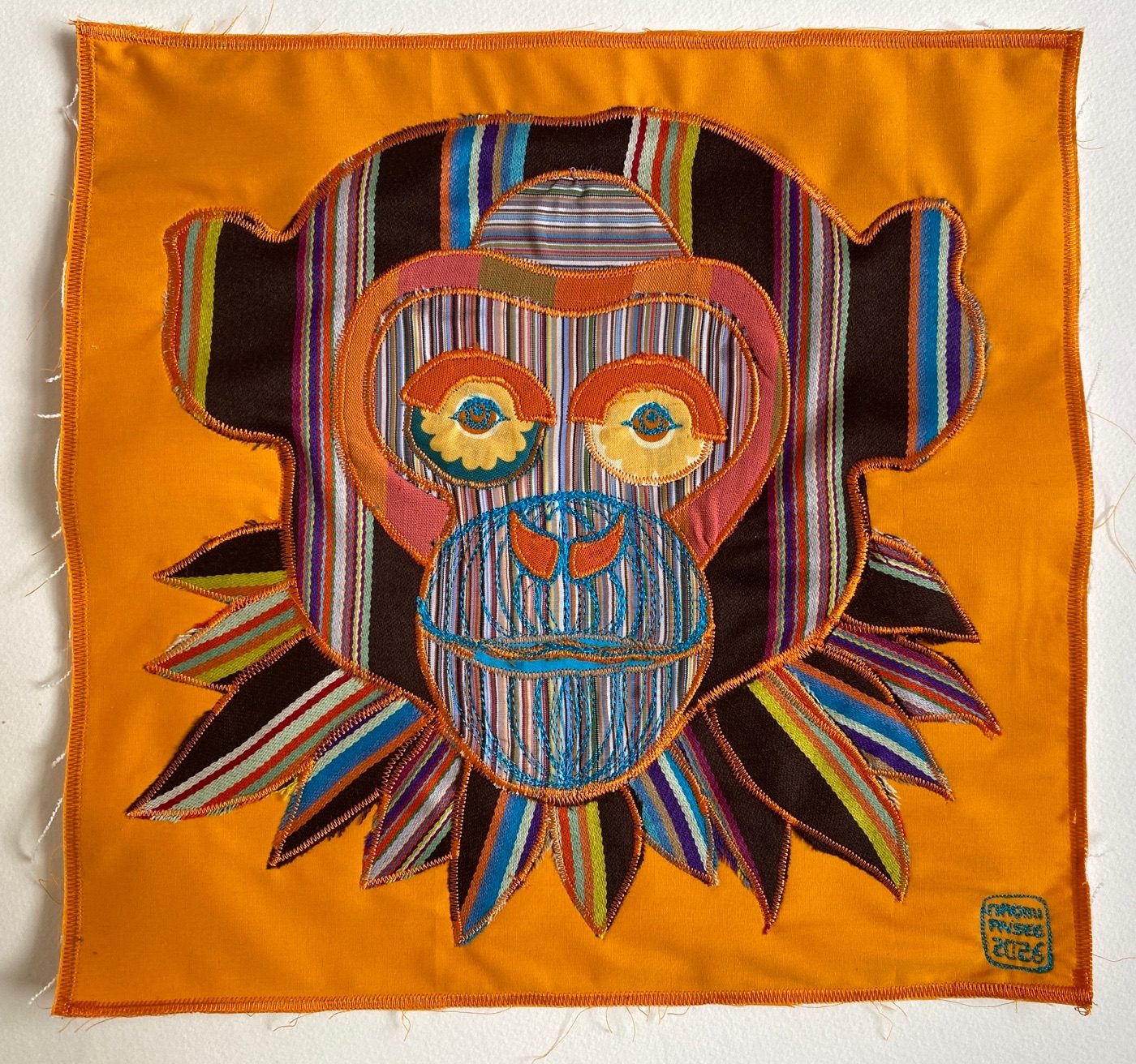 Orange fabric appliquéd and embroidered artwork of a chimp's head. Orange background and chimp made up of a selection of striped Paul Smith fabrics