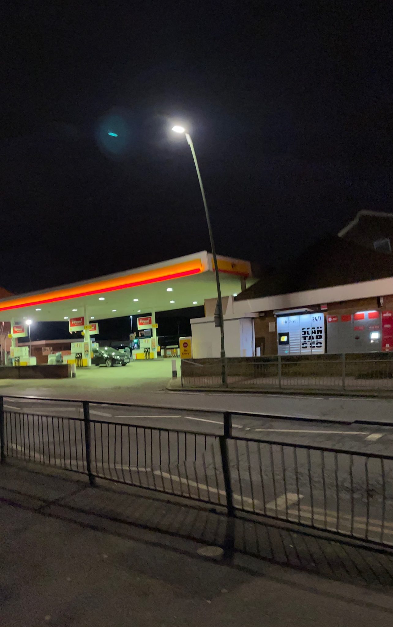 Night time photo of a street scene with a petrol station, a lamp and collection lockers