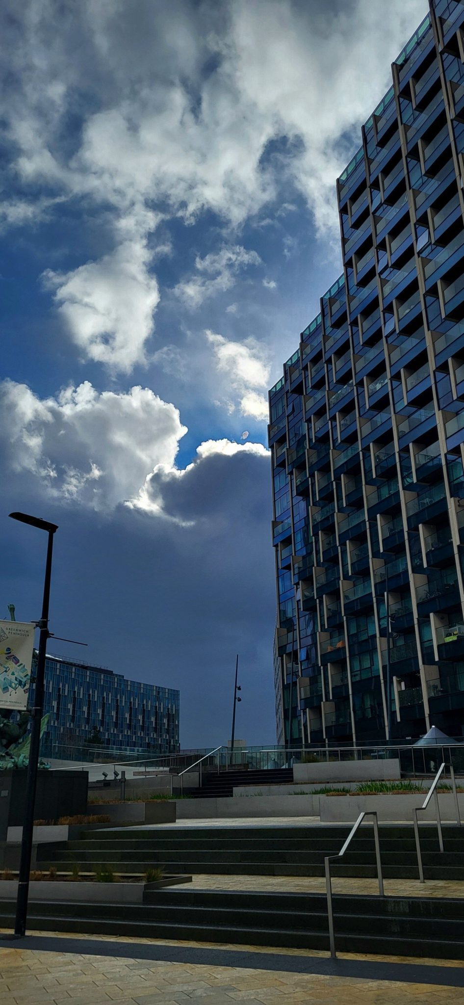 A photo of the sun bursting through clouds over a glass faced tower block