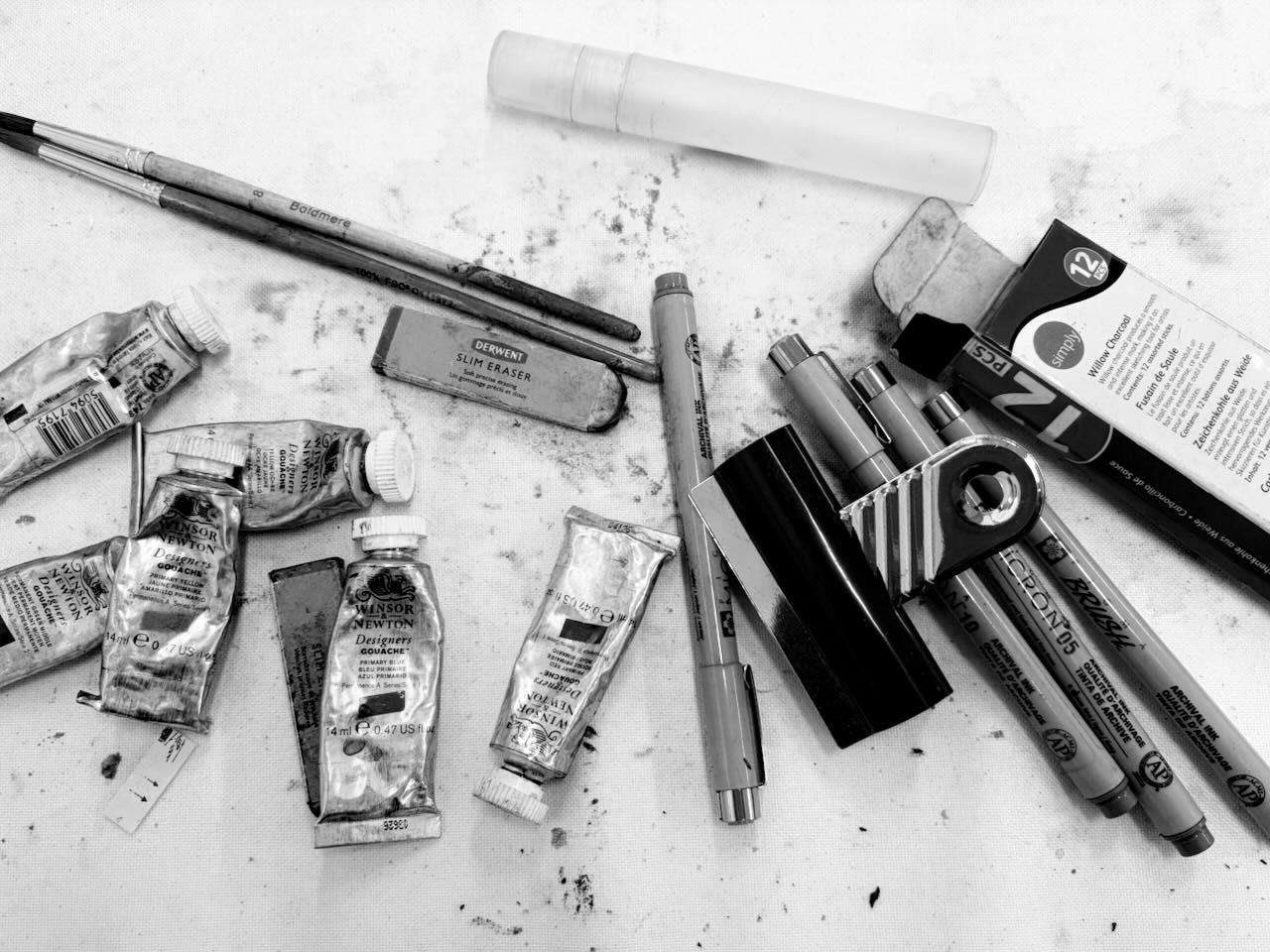 black and white photo of brushes, pens, rubber and charcoal pieces on a desk
