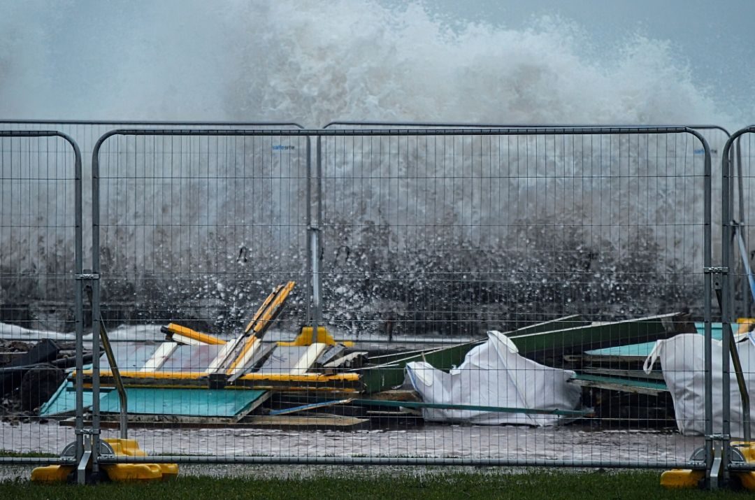 Waves crashing up above a sea wall. A pile of broken coloured wood.