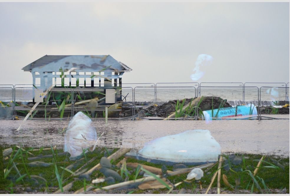 Beach shelter surrounded by water. Image of sea debris on grass superimposed ontop