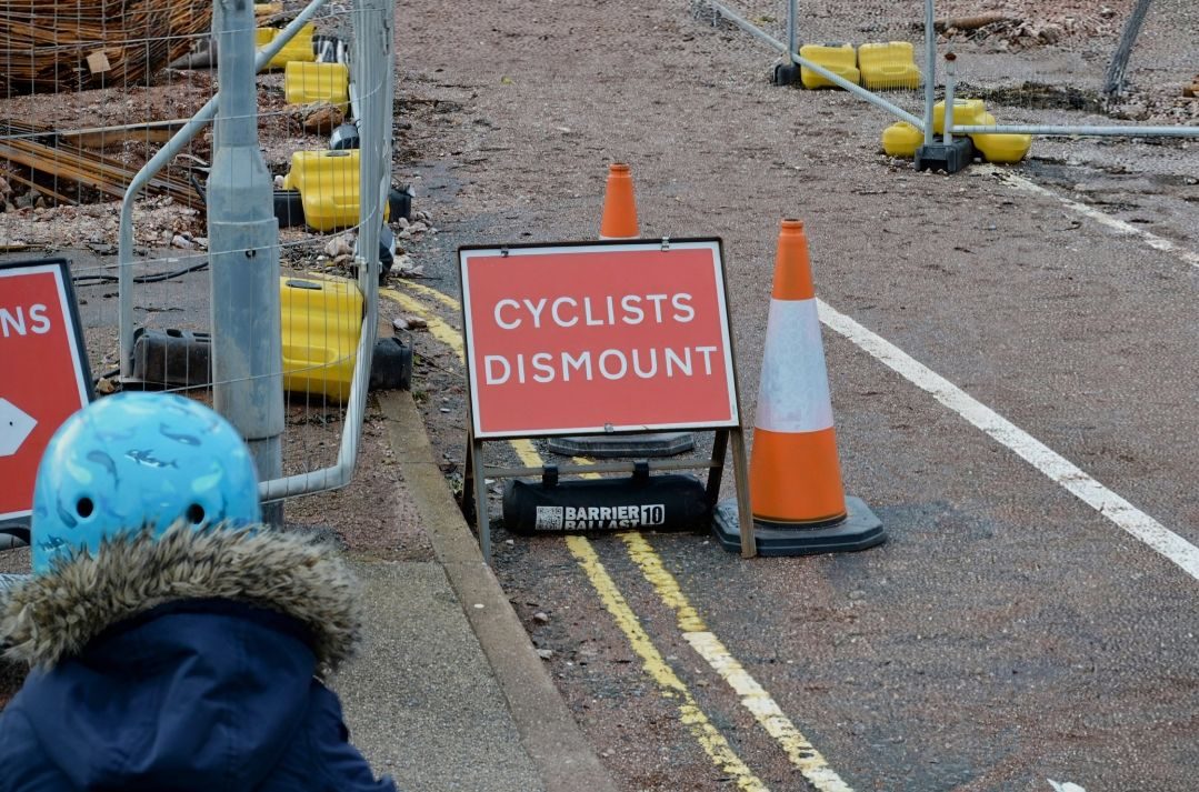 Cyclists dismount sign. Head and shoulders of a child in a helmet from behind.