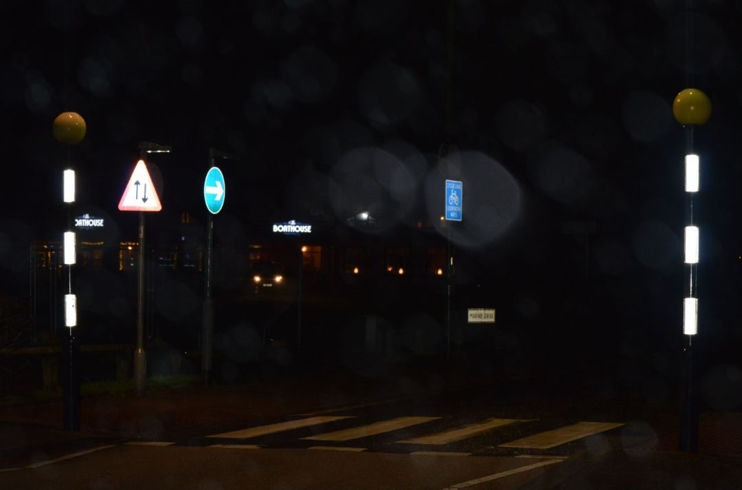 Nighttime scene. Reflections from street signs and zebra crossing poles