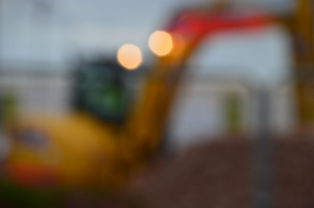 Blurred image of a dark yellow digging machine with lights on on a gray backgroubd