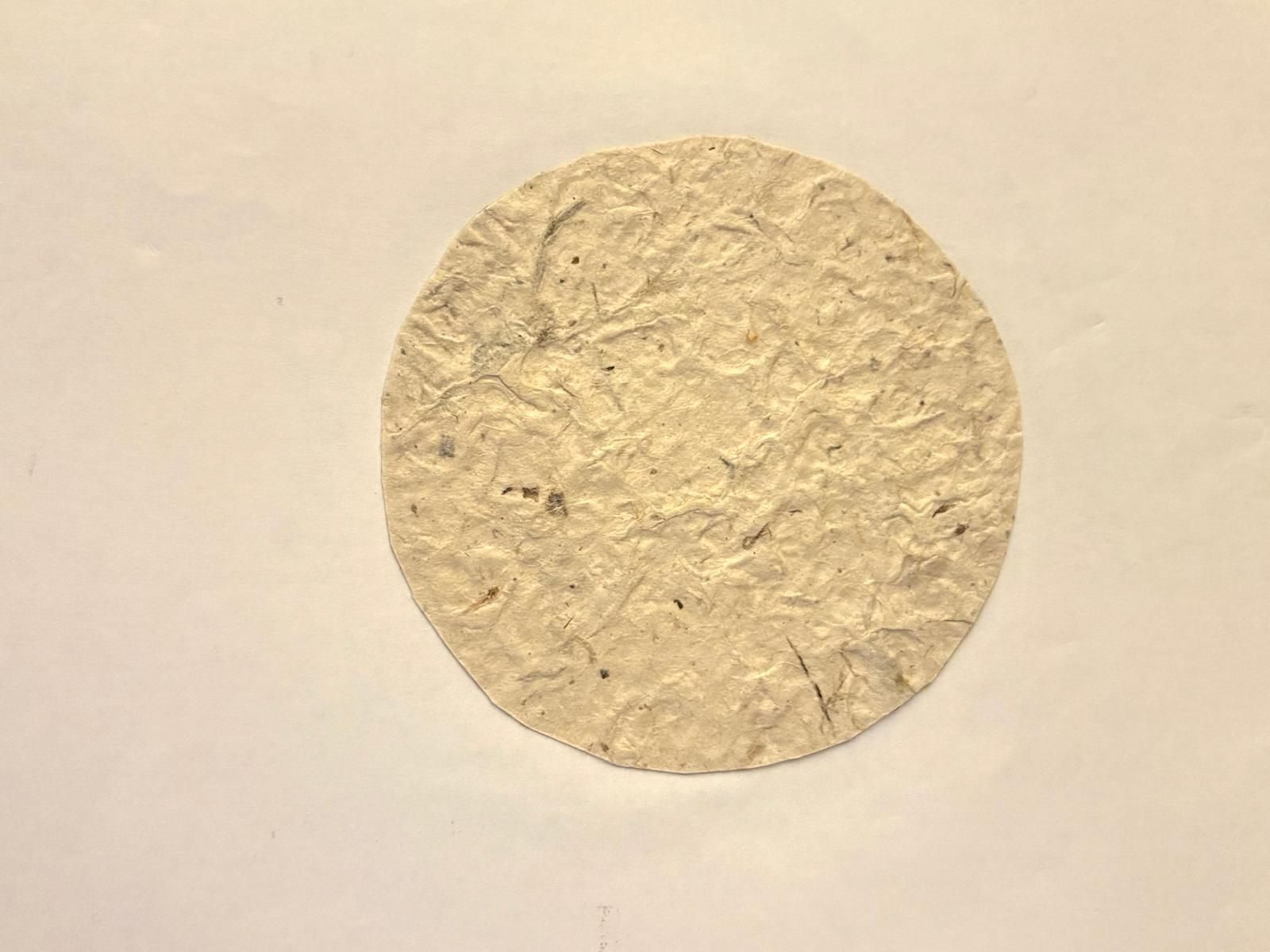 A grey textural circle stuck on white paper, similarly to the moon