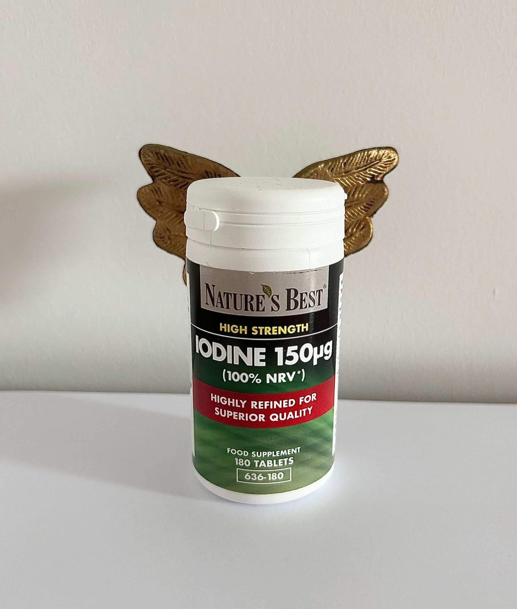 A small plastic container filled with an iodine supplement with a pair of golden angels wings (a Christmas Tree decoration) attached to the back. The Iodine appears as an angel.