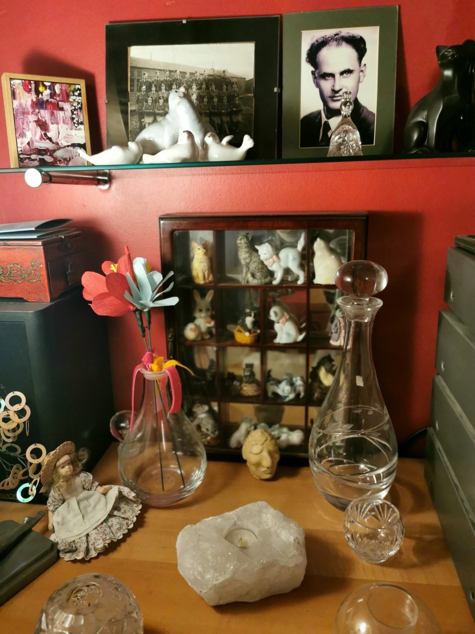 ornaments site on a sideboard and shelves including china cats in a glass box, ceramic sea lions, decanters, candle holders and old photos of family members