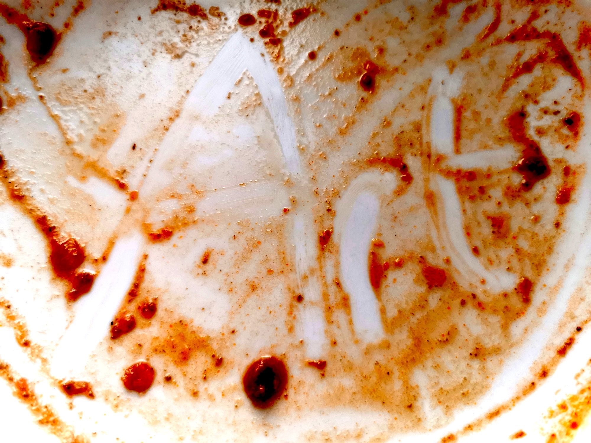 remains of spaghetti sauce in a white bowl with the word 'Art' written in it with a finger