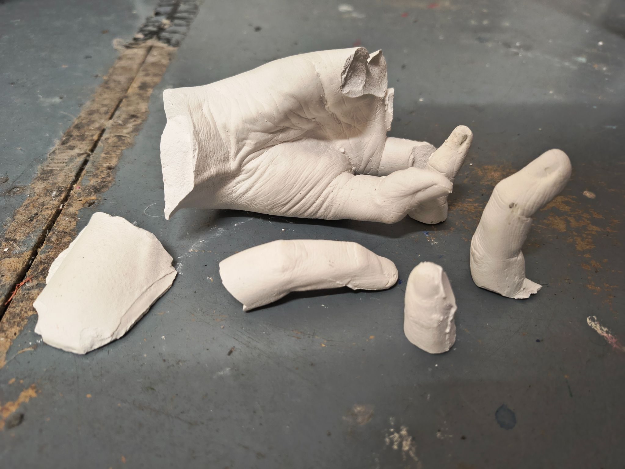 An image of a plaster cast hand on the floor that has been broken, the broken off fingers are placed round the main hand