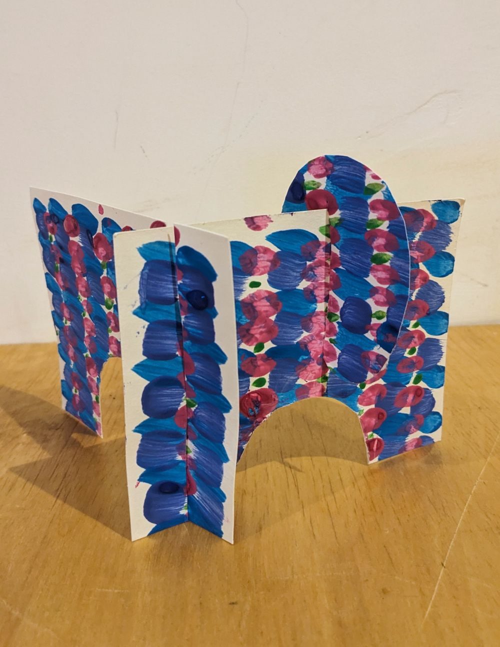 a purple and blue paper sculpture with two arches on a wooden table top