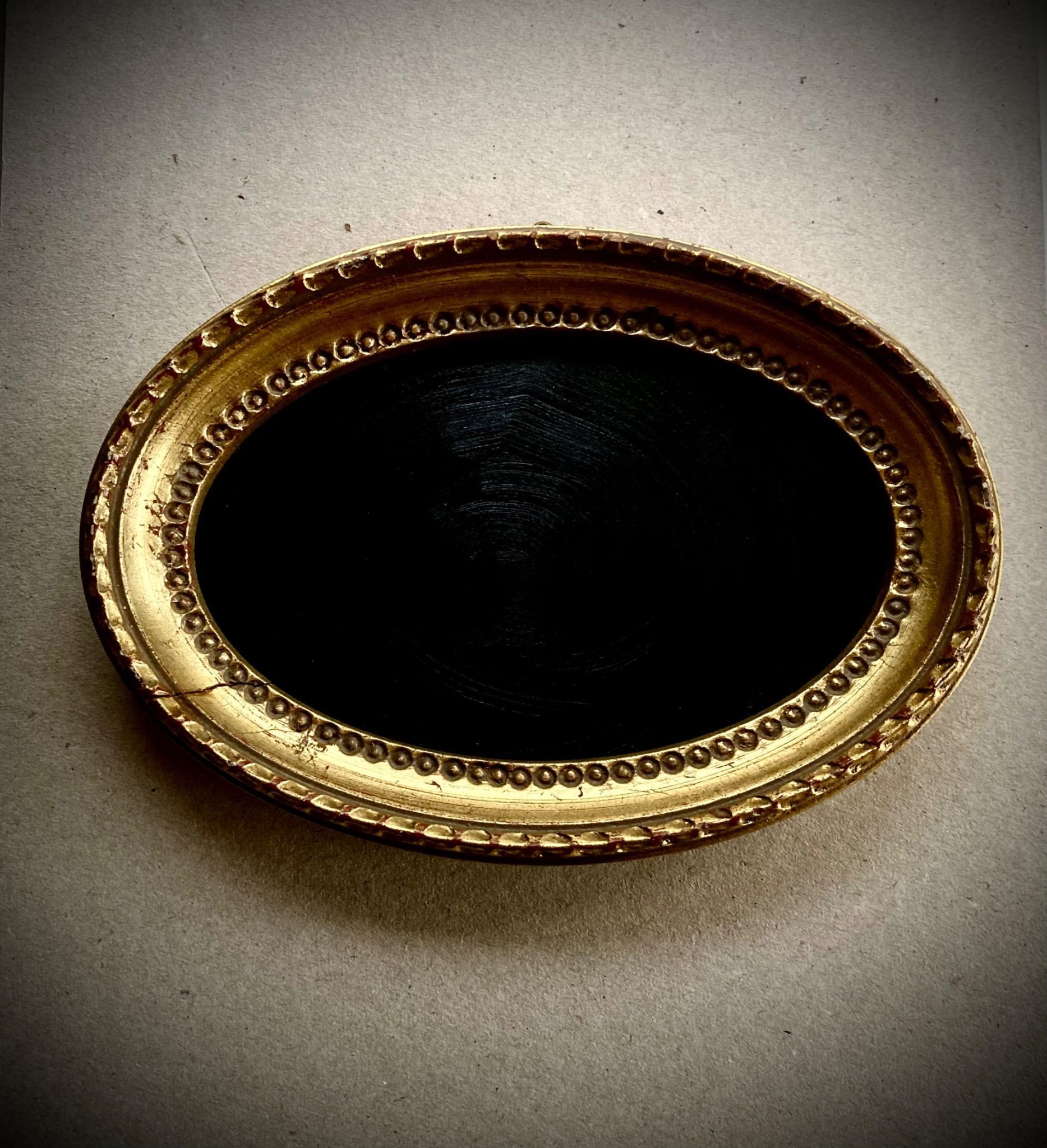 Gold antique oval picture frame containing black painted board, to be used as a divination device (such as Dr John Dee's black mirror). The oval-shaped frame also mimics the shape of an eye, which is symbolic of 'all-seeing'.