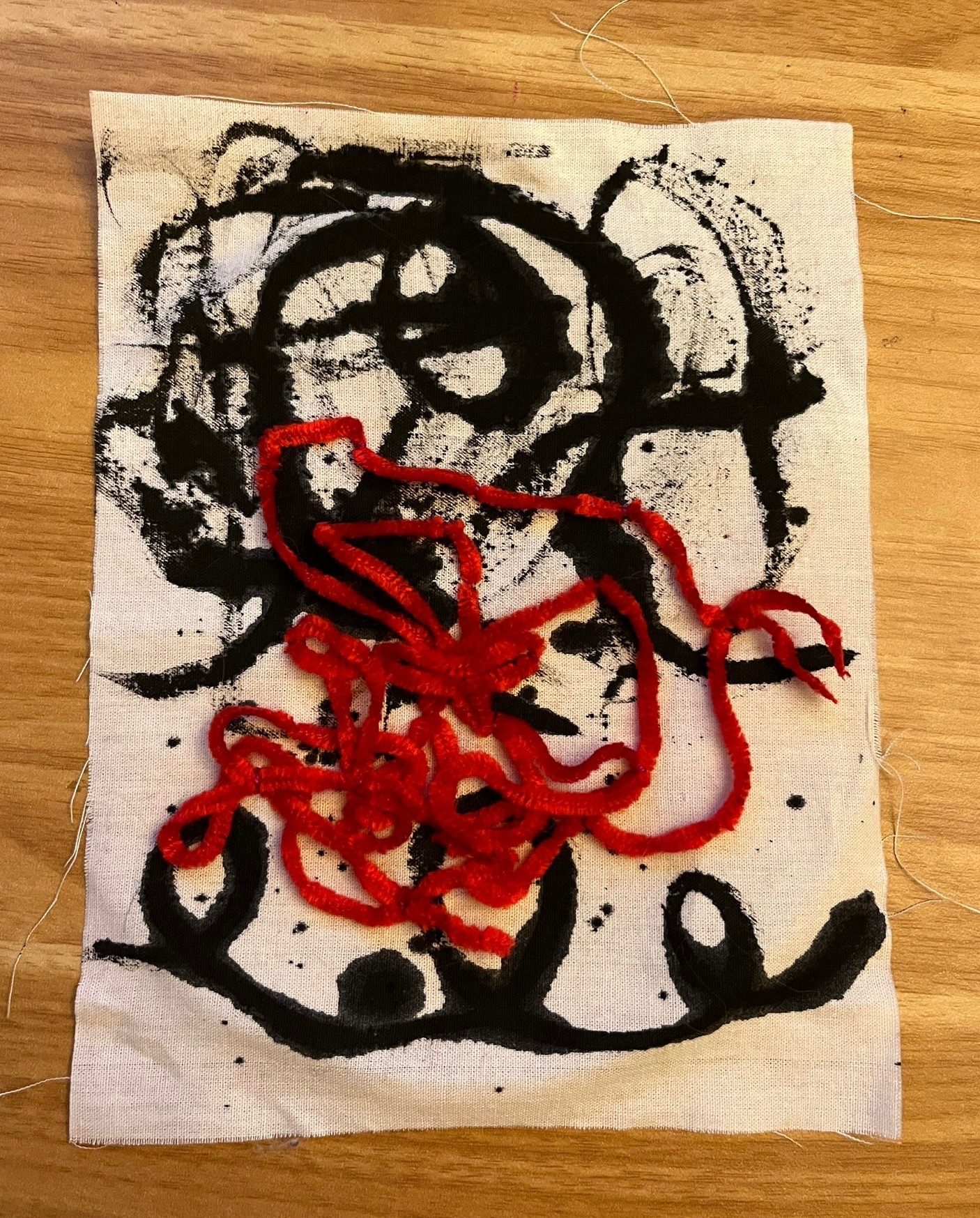 Black ink on white fabric with couched red textured thread in a tangle