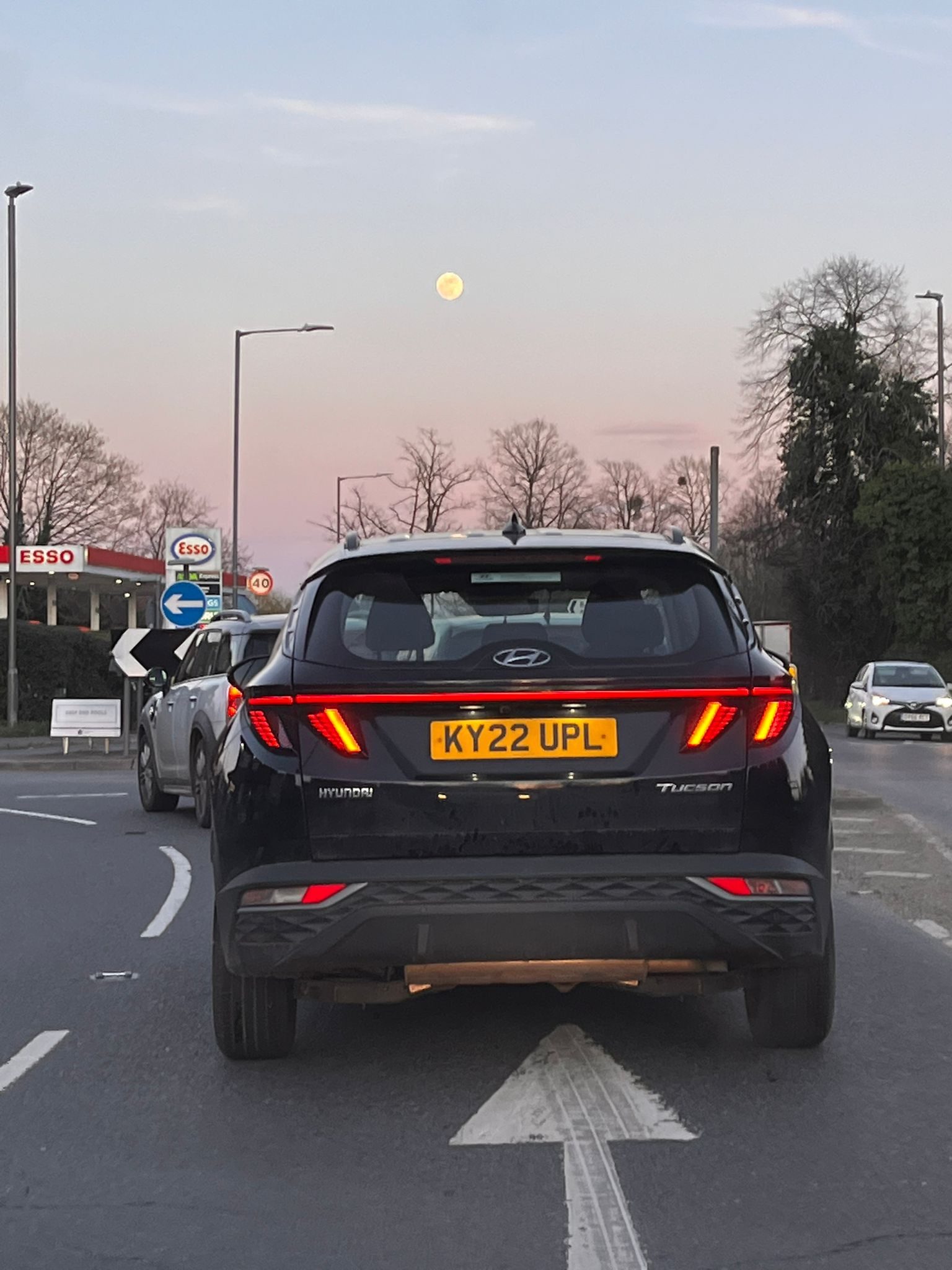 A busy roundabout, with the sunset and the full moon on the sky