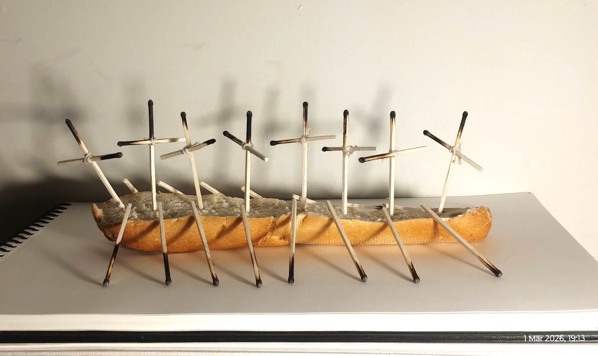 this is a sculpture made from bread, : a small bread boat containing matchstick figures.