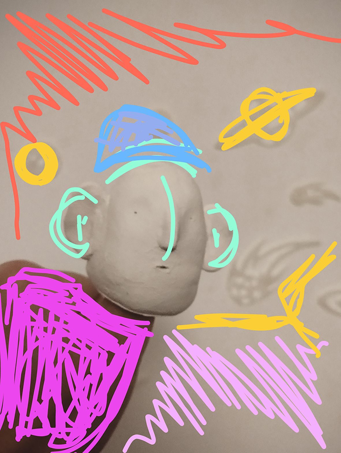 A photograph of a clay head, with colourful doodles surrounding it.