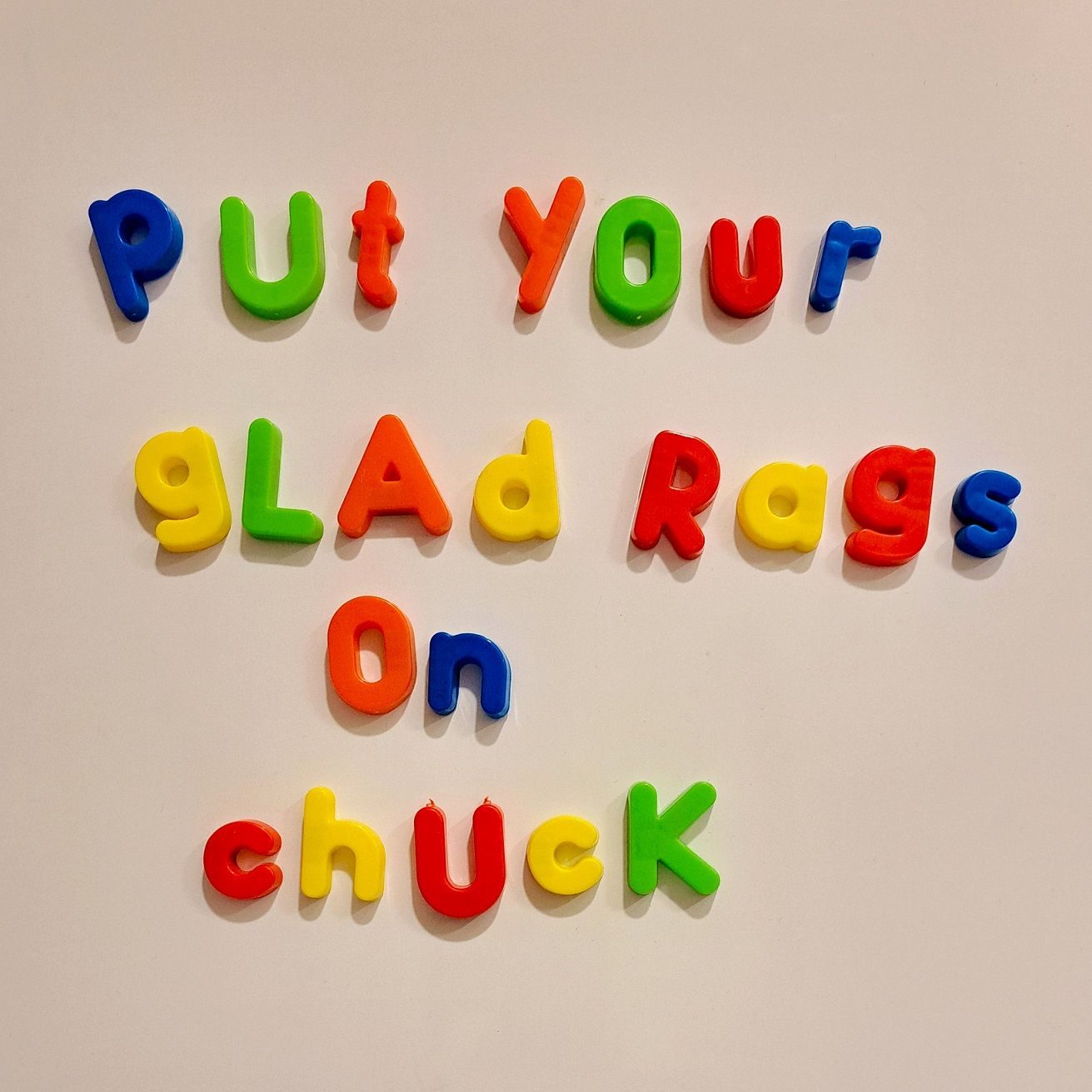 A square photo of colourful plastic letters with magnets on a fridge, spelling out 