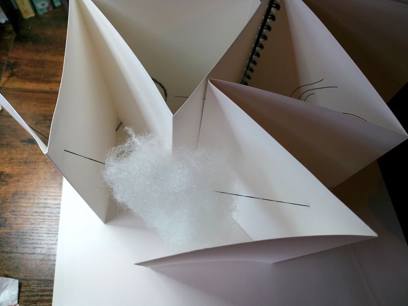 view from above of a cloud suspended between different pages of a concertina sketchbook, mixed media