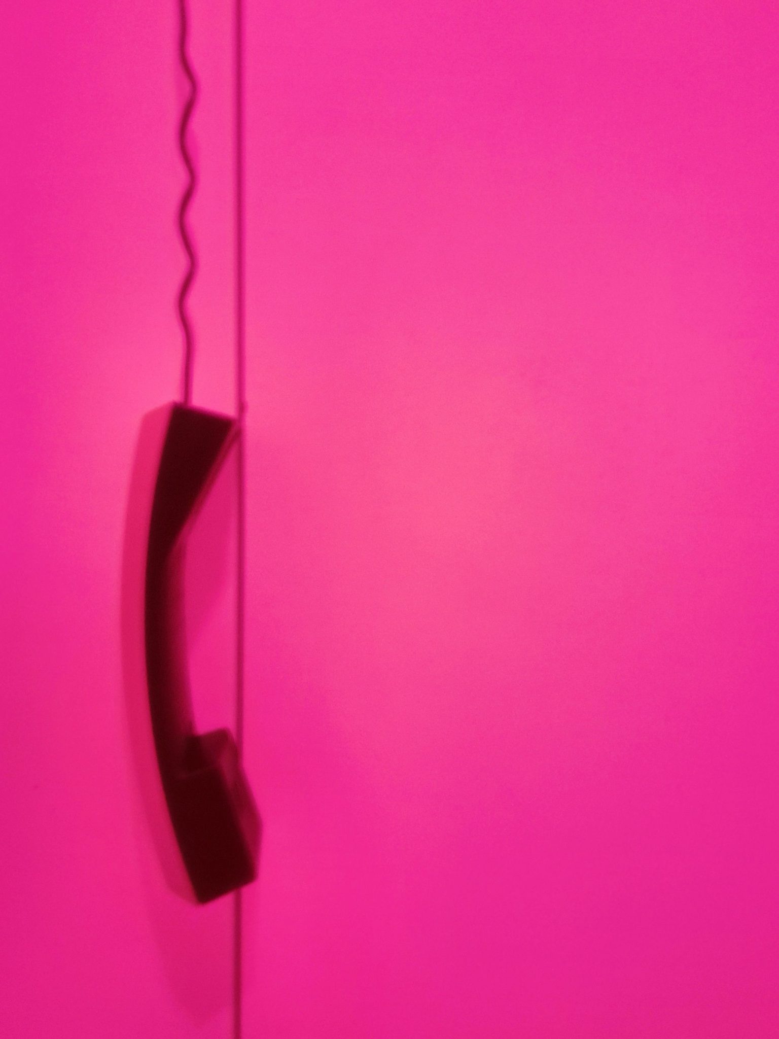 A photo of an old-fashioned phone hanging from its cord. Everything appears to be pink.