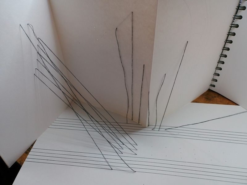 abstract drawing with black thread stretching from bottom paper to pages of concertina sketchbook next to it
