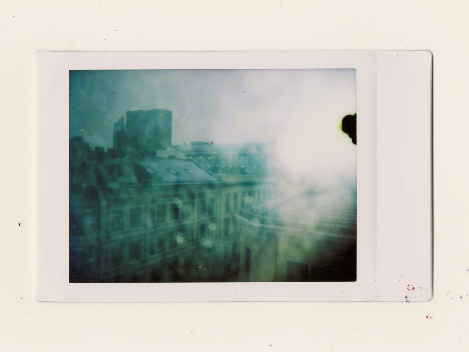 A faded polaroid image of a cityscape. There's a chemical leak near the top right corner. It appears to be raining.