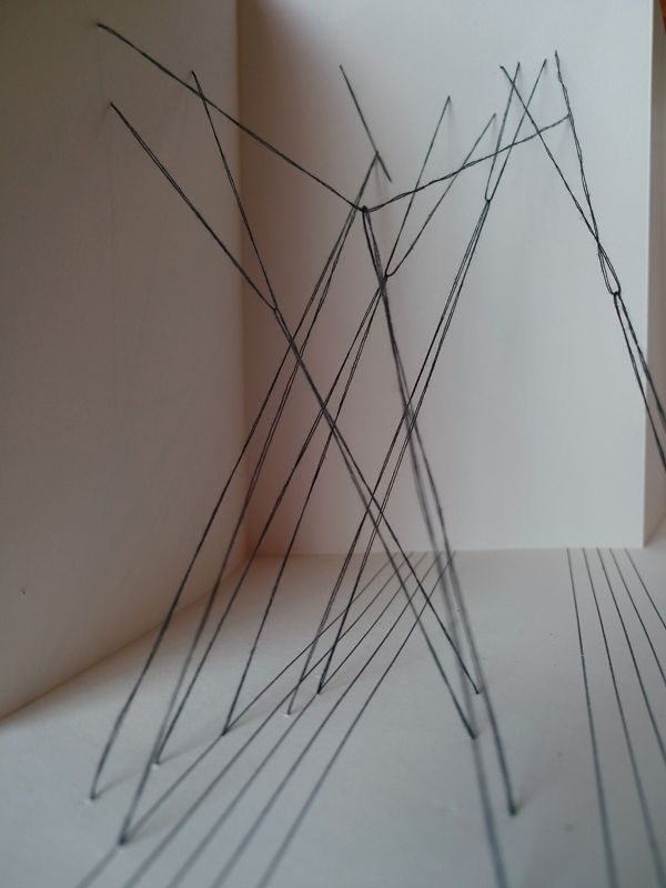 drawing in strands of black thread suspended from a stave on the bottom towards a page of a concertina sketchbook