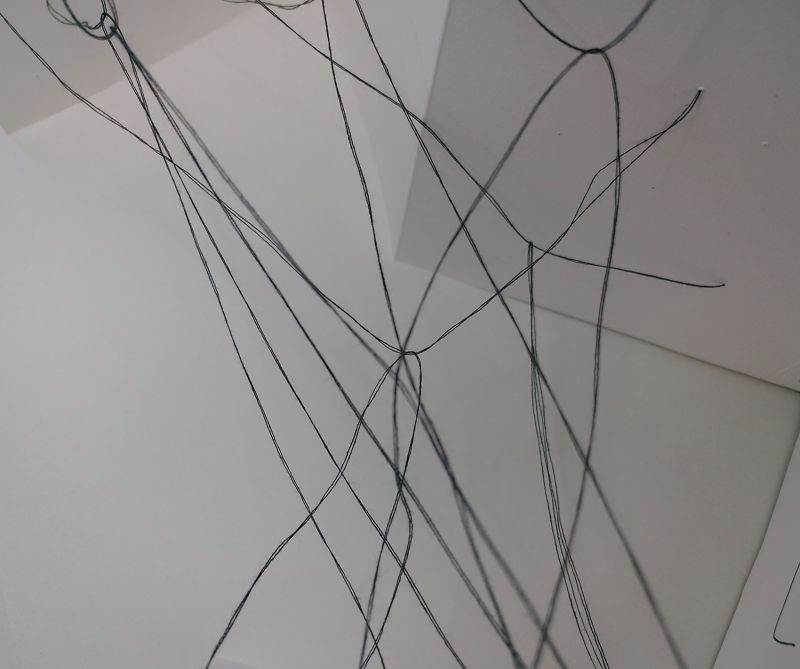 abstract drawing with black thread suspended between pages of a concertina sketchbook, some are tauter than others