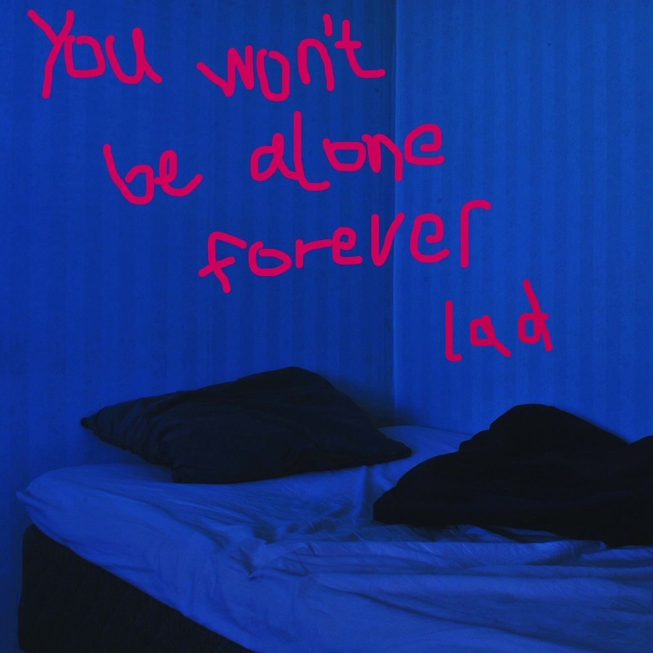 A grainy photo of an unmade bed in a blue room, it appears to be nighttime. Written on top in messy neon pink, it says 