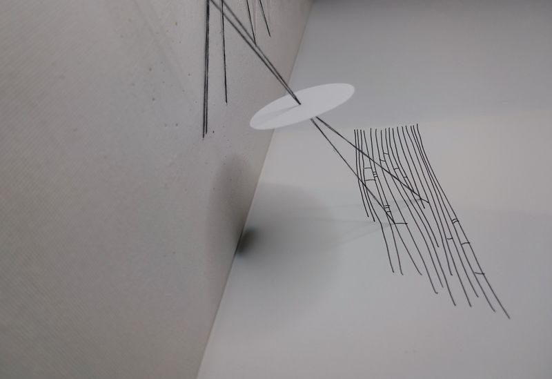 A paper circle suspended with black thread between drawing in black pen and canvas