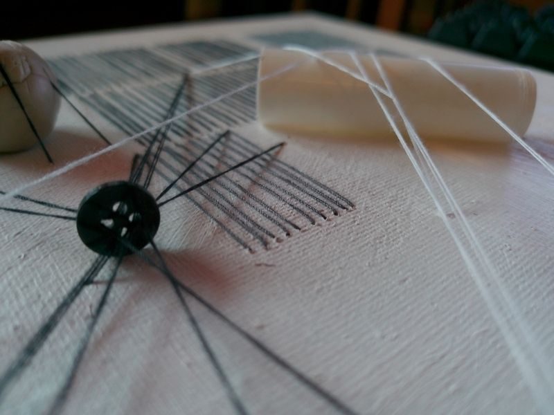 Abstract embroidery with a black button and a plastic white bobbin sewn onto canvas, casting shadows