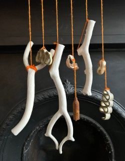 A row of hanging pieces of broken slip casts that look like branches interspersed with objects from the beach a stone and a shell, and a rusty capsule