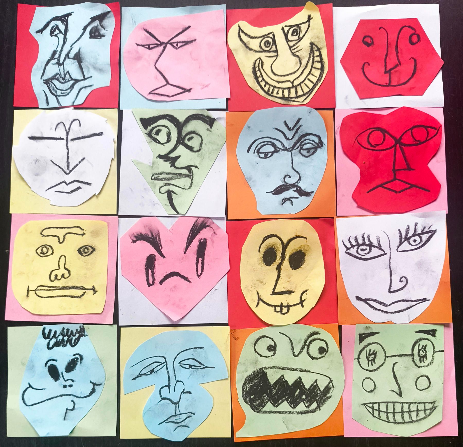 16 cartoonish faces, drawn in charcoal on notepad paper