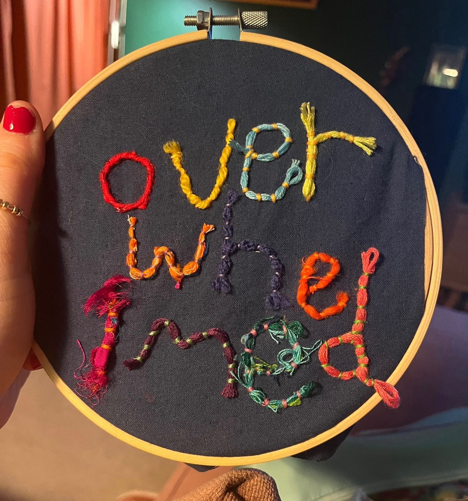 The word ‘overwhelmed’ in different embroidery threads sewn onto a dark blue background