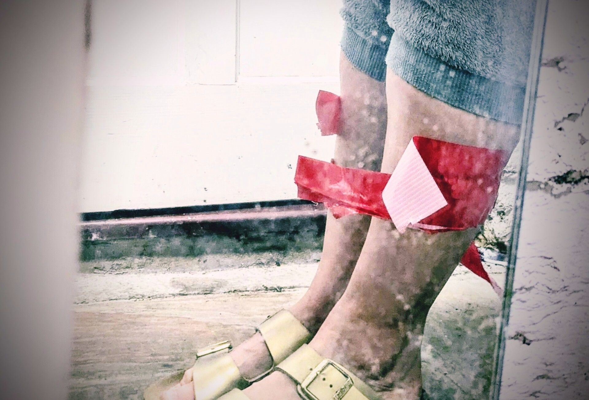 a picture of calves, bits of birkenstock and bits of pyjama bottoms, red gaffa tape around calves, a bit ripped open but still on the calves, trapping the person