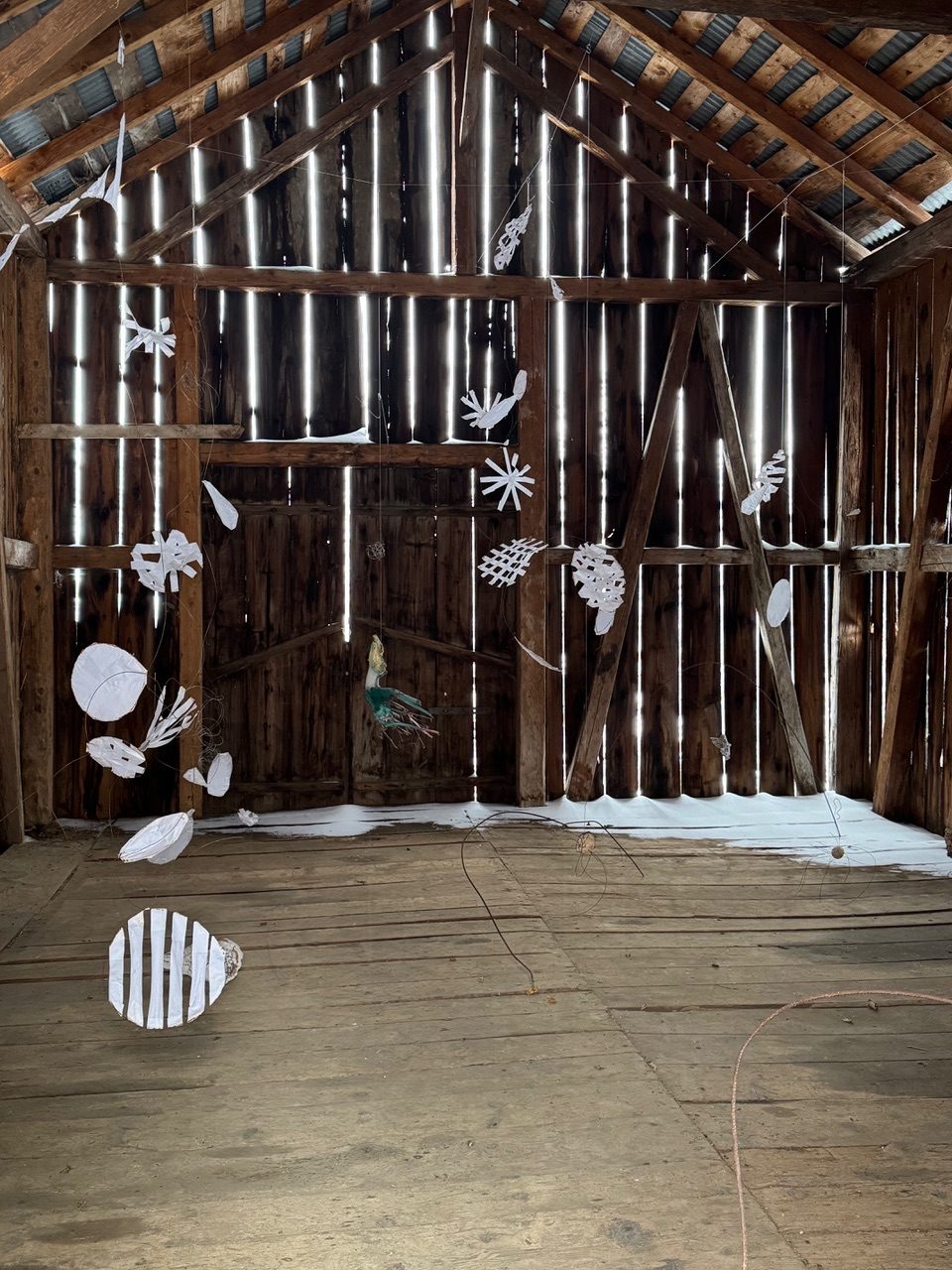 installation with  paper and wire shapes hanged in a barn with recycled metal pieces and painted wood. The snow entered through the wooden gaps of the barn
